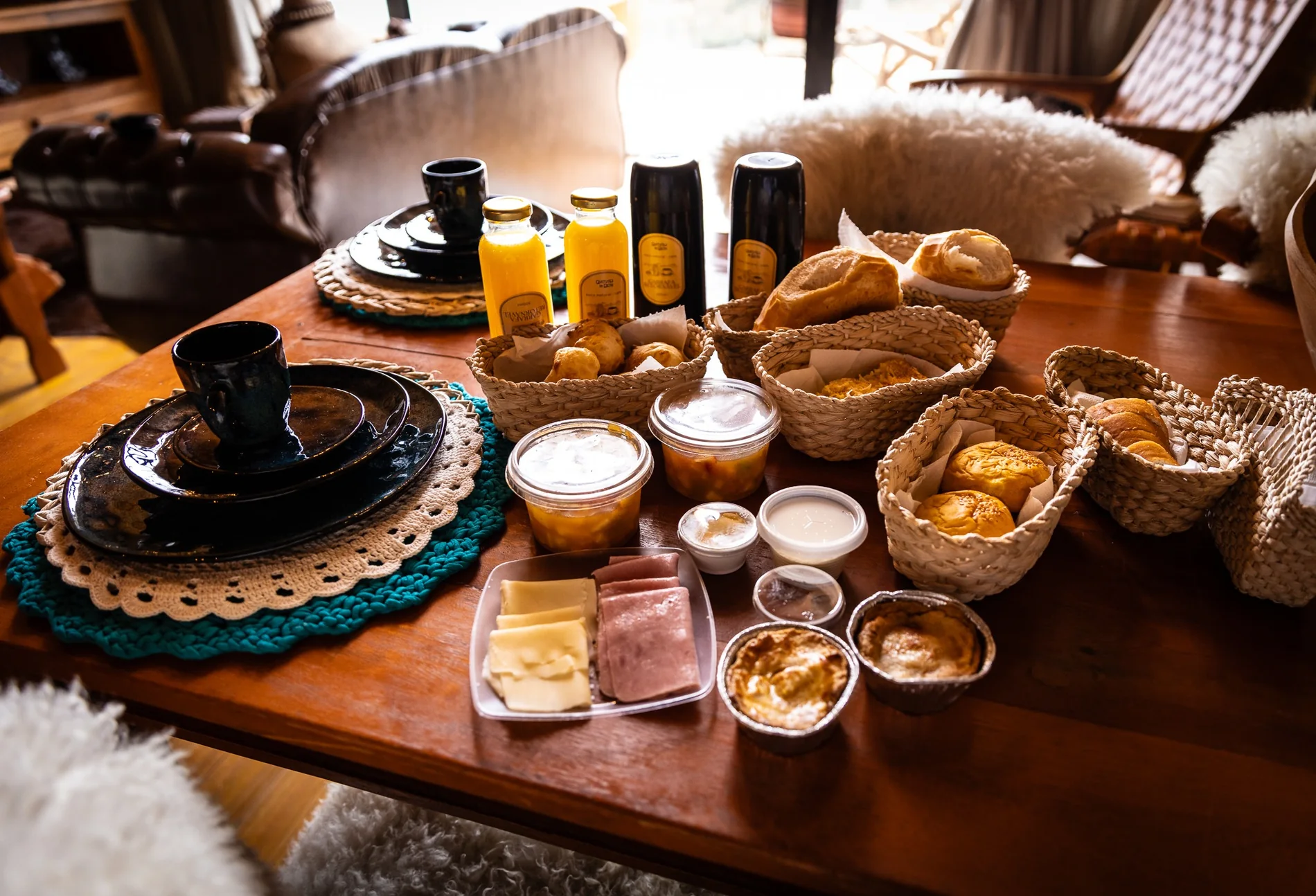 Café da manhã na cabana, com pães em cestas, frutas, queijos e bebidas sobre a mesa